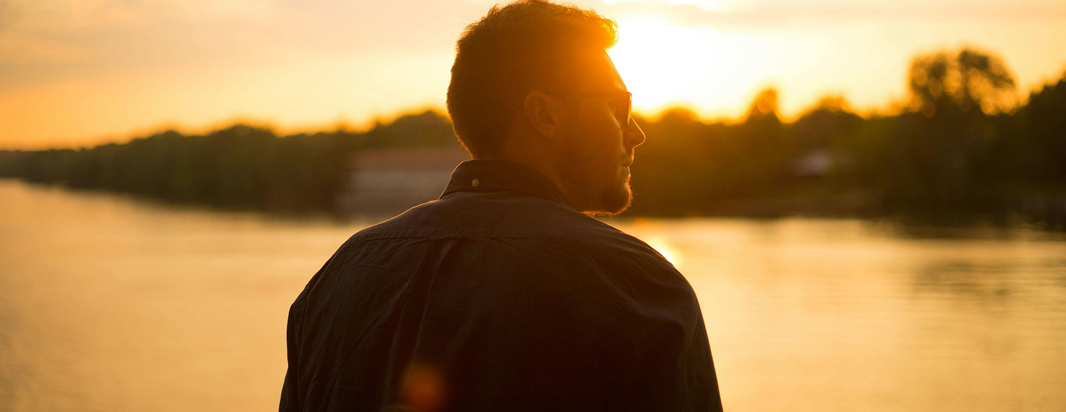 A man staring into the sunset across a lake