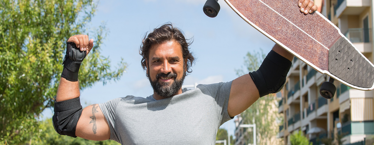 A beared man holding up a skateboard