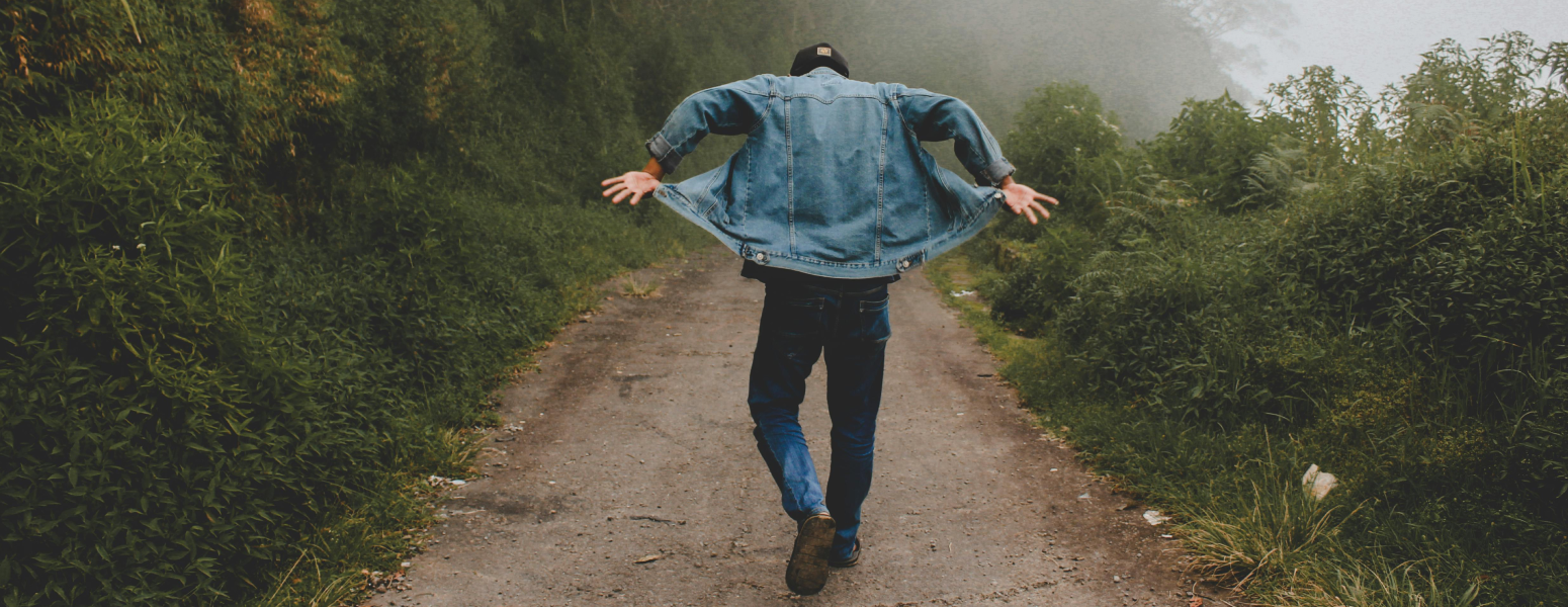  a man in a denim jacket walking through some woods